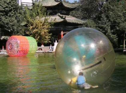 In the People’s Park a boy trapped in a giant beach ball approaches a giant hair curler and certain disaster